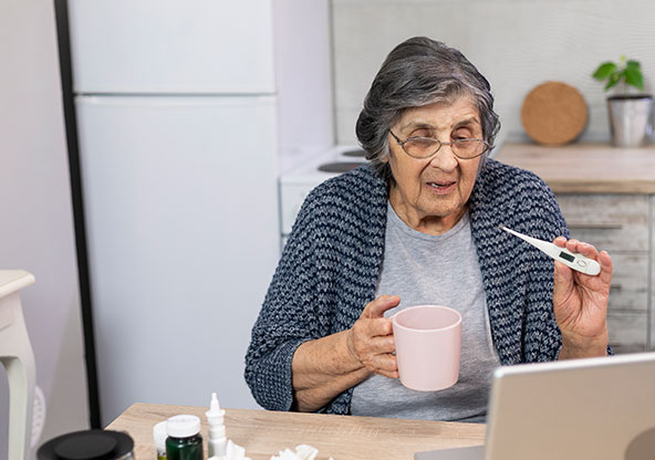 Senior Woman holding thermometer towards computer. She is getting virtual care for fever and cough.