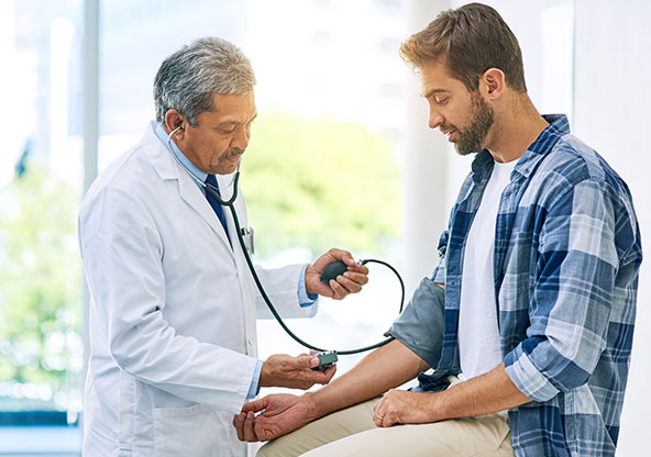 A doctor measures a man’s blood pressure during a routine medical exam in a clinic room.